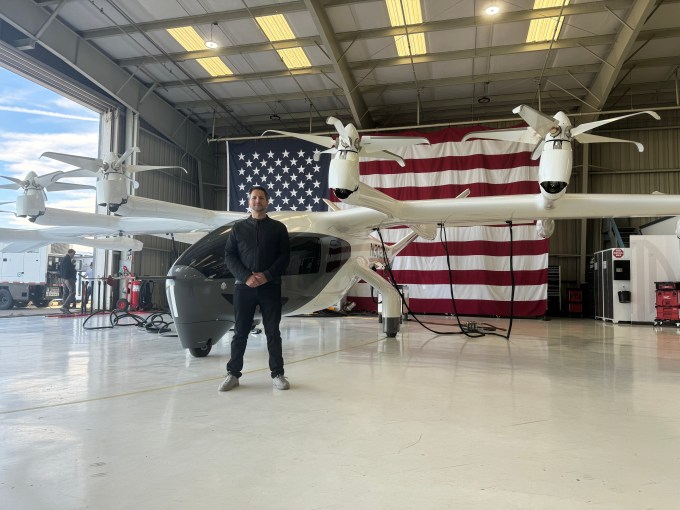 Adam Goldstein, PDG d'Archer, se tient avec l'un des EVTOL de son entreprise devant un drapeau américain géant.